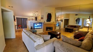 Uma sala de estar com sofá, televisão, lareira e um espaço de refeições com cadeira e mesa.