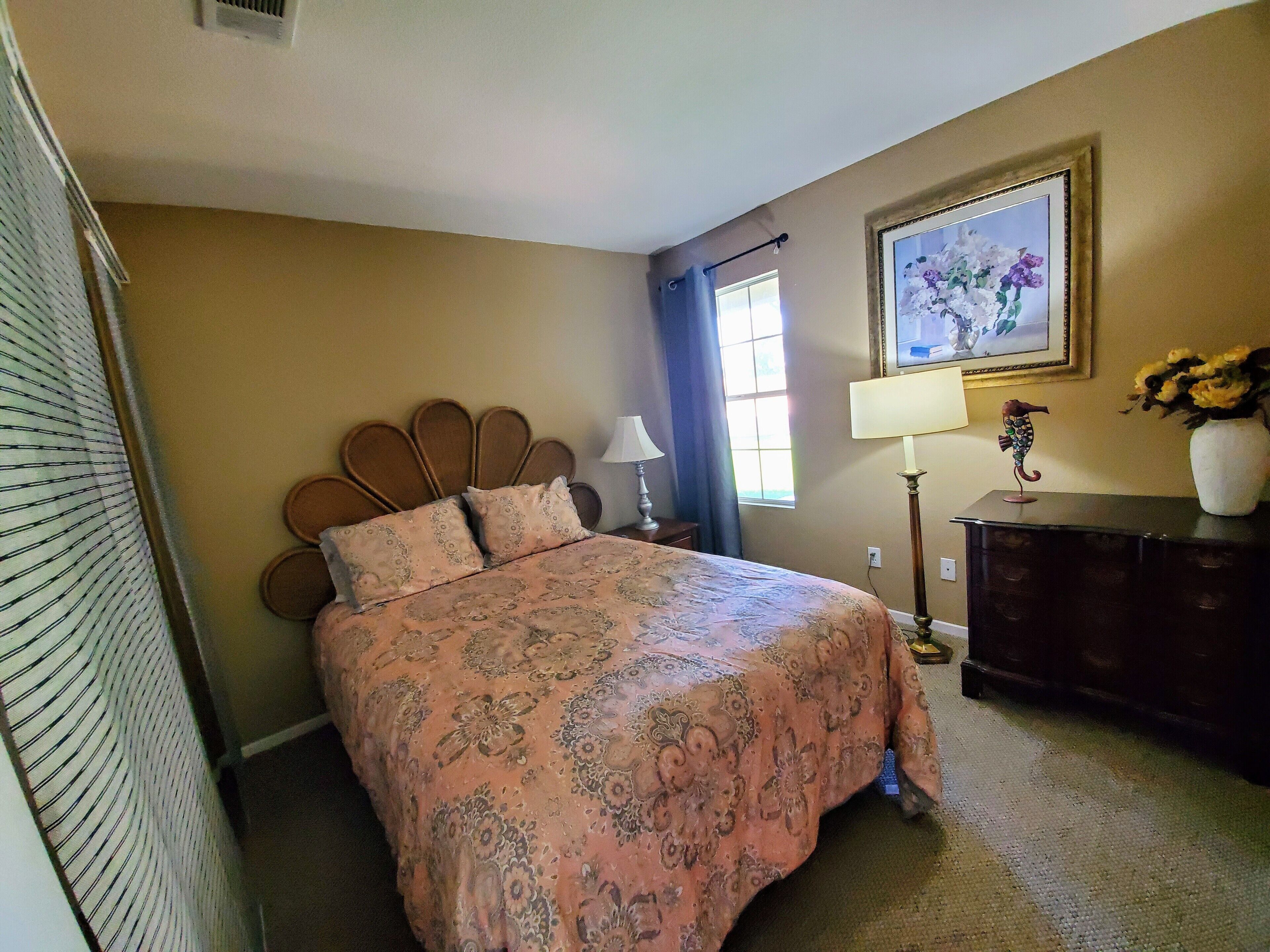 A bedroom with a bed, a nightstand, a lamp, a dresser, a window with curtains, and a framed picture on the wall.
