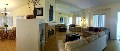 A spacious living room with a large sofa, a dining area with wicker chairs, and a kitchen area with a refrigerator and microwave.