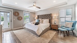 A bedroom with a large bed, a ceiling fan, a nightstand, a chair, and a window with blinds. - 122 Luxury Hilton Head Beach House w/ Heated Pool & Elevator (Hilton Head Island)