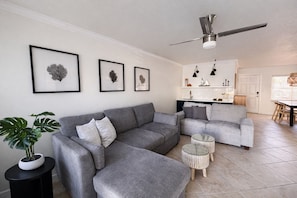 Un salon moderne avec un canapé d’angle gris, une petite table ronde et une plante en pot.