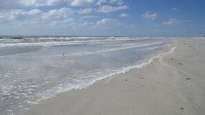 A beach with gentle waves and a clear sky. - Modern Barefoot Beach 2BR Condo, Steps to Beach & Pool (Indian Shores)