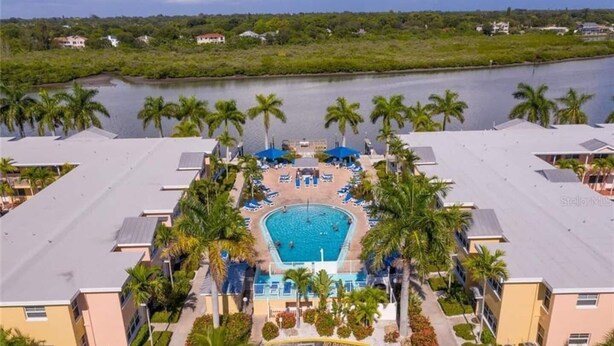 A resort with a central swimming pool surrounded by palm trees and lounge chairs. - Modern Barefoot Beach 2BR Condo, Steps to Beach & Pool (Indian Shores)