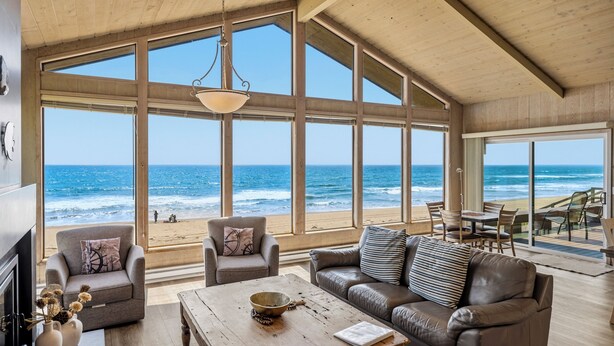 Un salón amplio con ventanas grandes con vistas a la playa, una chimenea y un comedor.