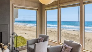 Una habitación con ventanas amplias que dan a una playa, chimenea y dos sillones.