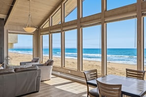 Ein Zimmer mit großen Fenstern und Blick auf einen Strand, möbliert mit einer Couch, Sesseln und einem Tisch.
