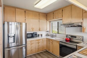 A modern kitchen with wooden cabinets, stainless steel appliances, and a window providing natural light. - House 98 - Ocean View (Watsonville)