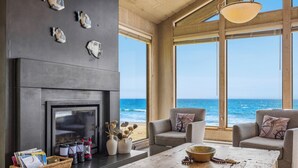 Una sala de estar moderna con chimenea, ventanas amplias con vistas al océano y asientos cómodos.