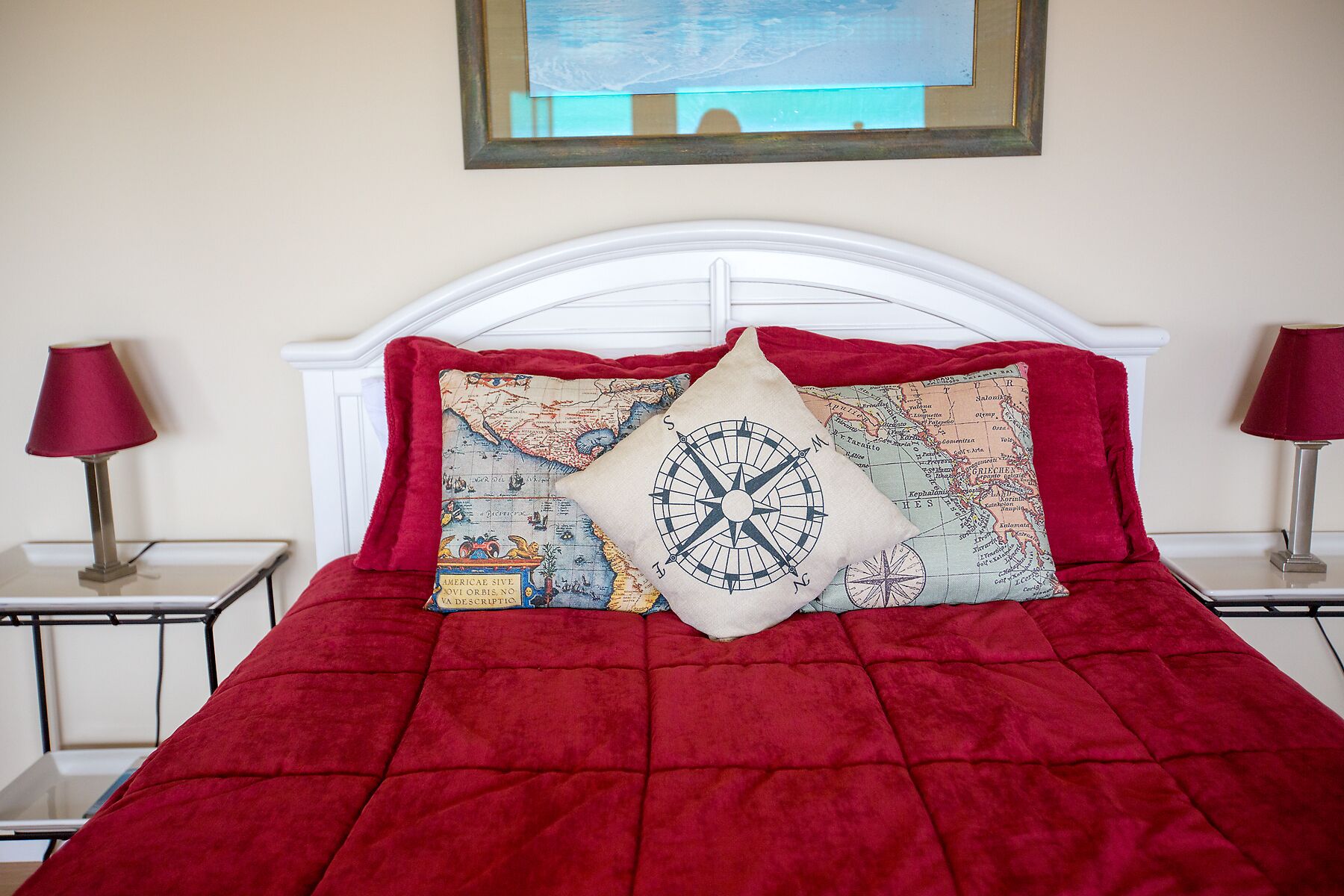 A bed with a red quilt and two decorative pillows, one with a compass design and another with a map pattern.