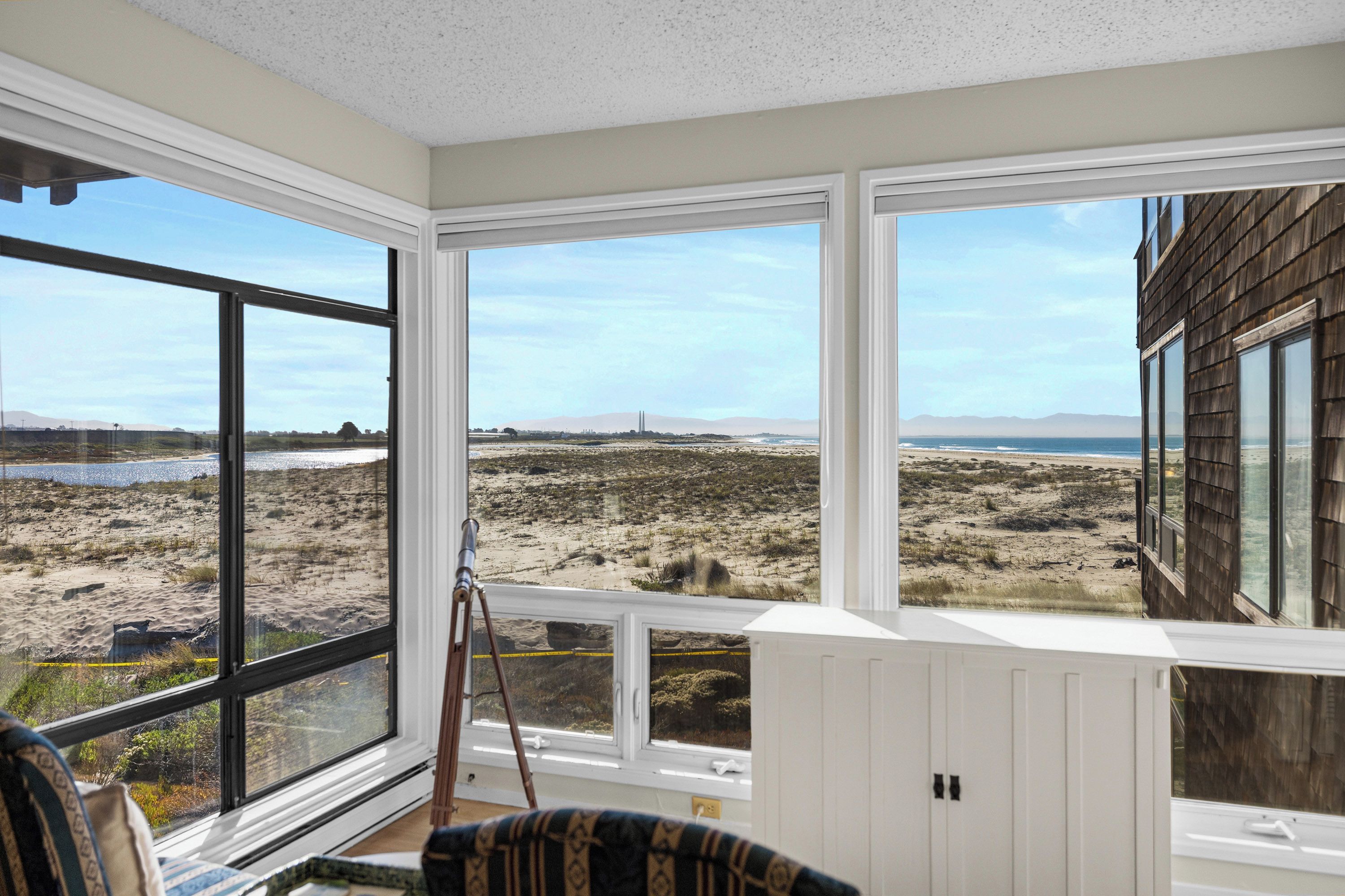 A room with large windows offering a view of a beach and distant mountains.