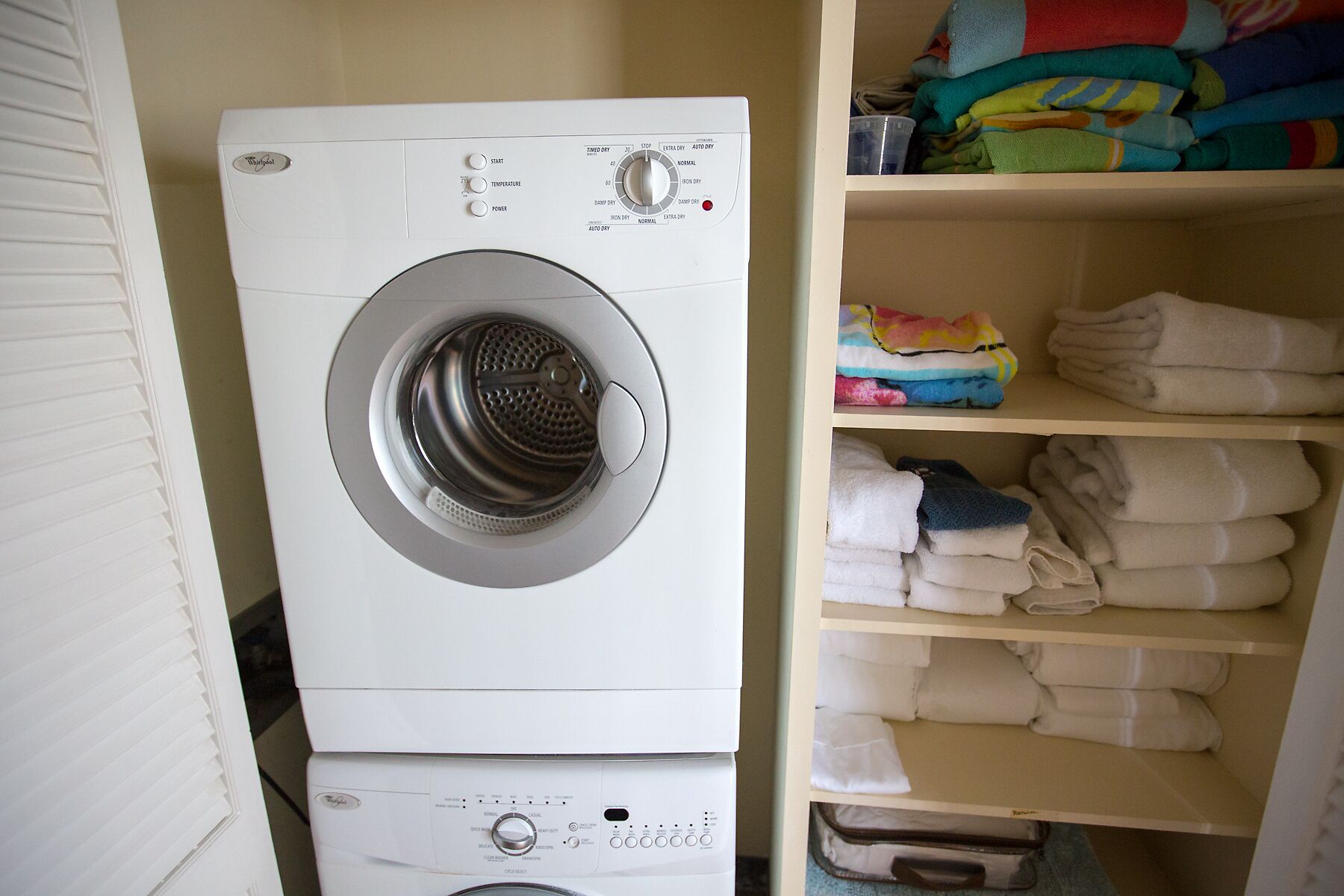 A front-loading washing machine with a control panel, a shelf with folded towels, and a wall-mounted shelf with folded towels.