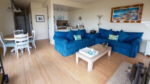 Een woonkamer met twee blauwe banken, een houten salontafel en een eethoek met witte stoelen.