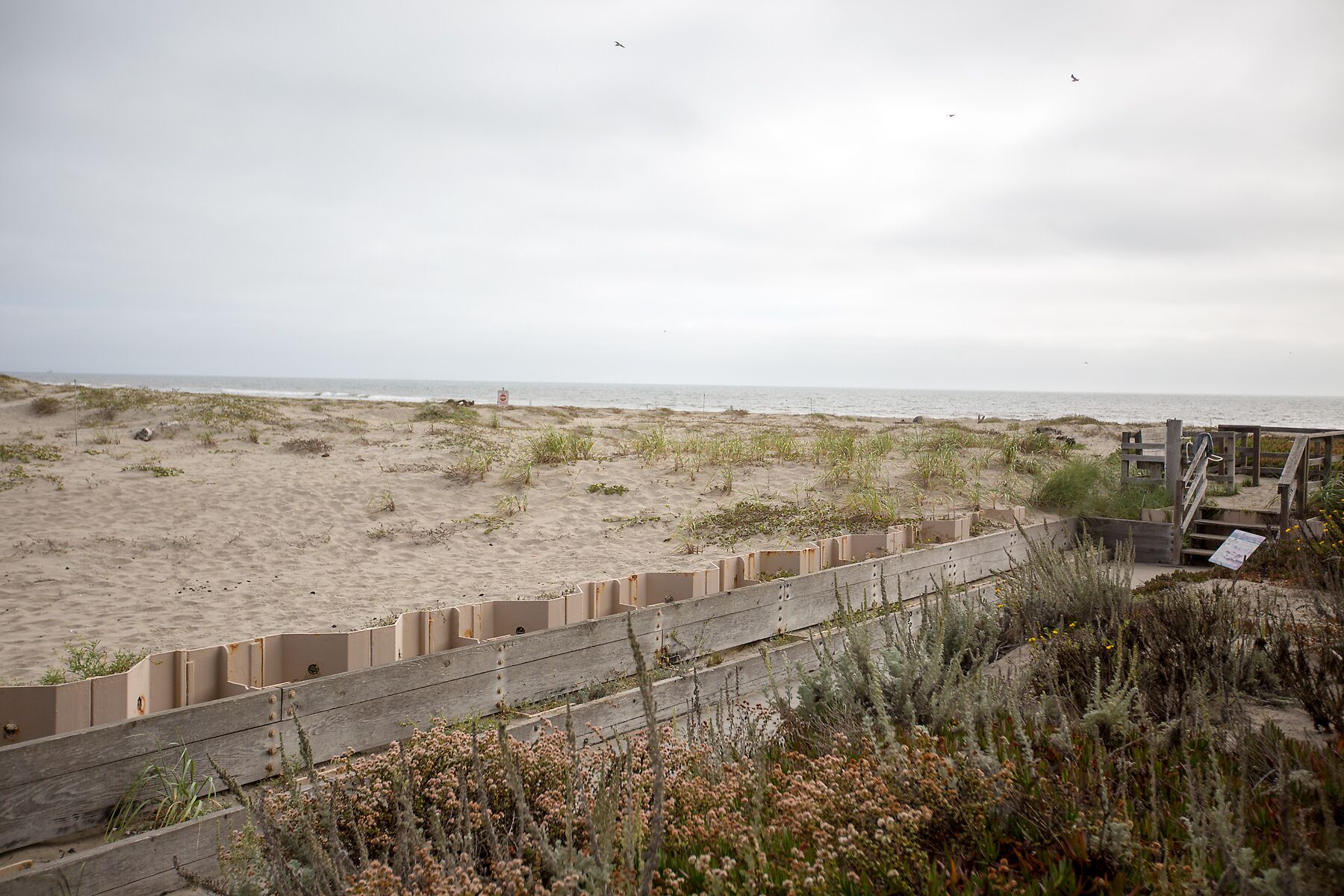 Une plage bordée d’une clôture en bois et d’une promenade qui mène à l’eau.
