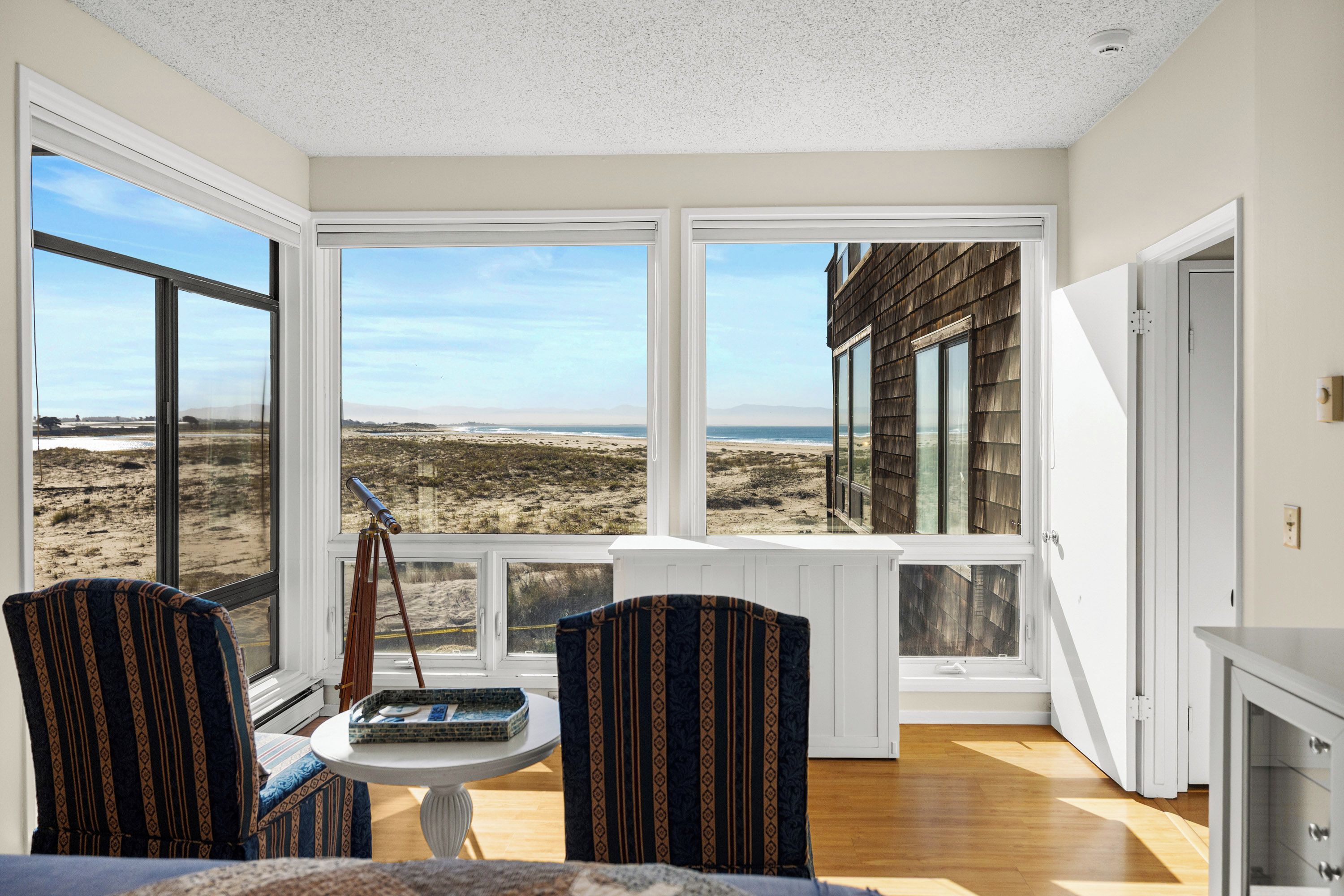 A room with large windows, a telescope, and a view of the beach.