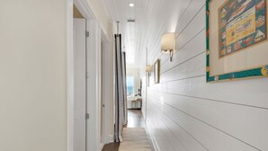 A hallway with white walls, a wooden floor, and a rug leading to a room with a view.