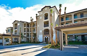 Stunning hotel with Mediterranean architecture, featuring balconies and a covered entrance, set amidst lush palm trees and a manicured lawn.