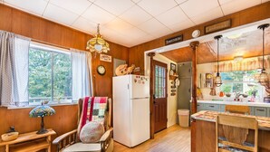 A cozy kitchen with wooden walls, a refrigerator, a dining table, and a window with curtains.