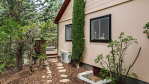 A house with a wooden deck, a stone pathway, and a tall evergreen shrub.