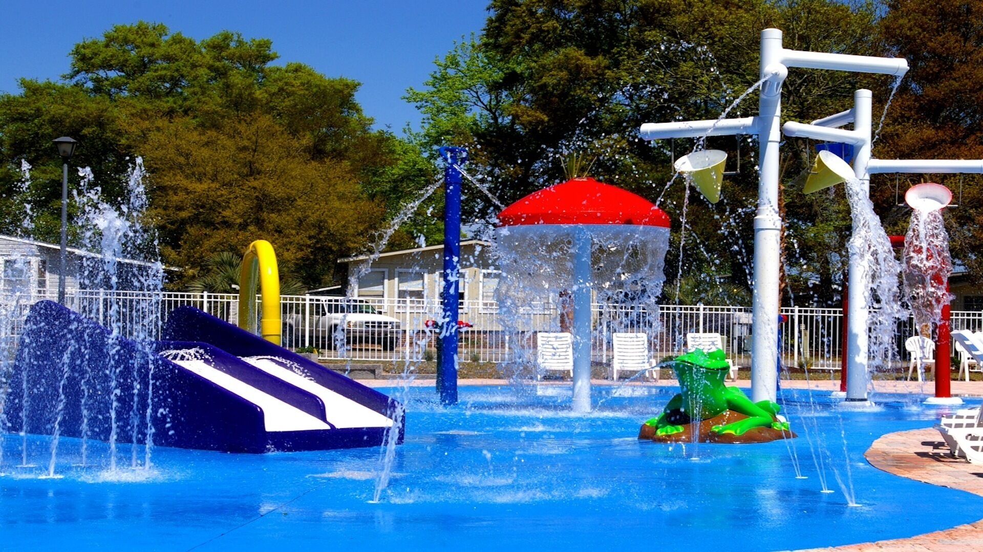 A water park with various water features including a slide, a green dinosaur float, and multiple water jets.
