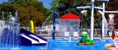 A water park with various water features including a slide, a green dinosaur float, and multiple water jets.