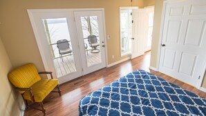 A bedroom with a bed, a yellow chair, and a sliding glass door leading to an outdoor patio. - Bridgeview Cottage with Weekday Pontoon Boat Access, and Quiet Peninsula Setting (Cadiz)