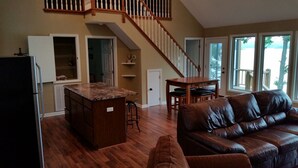 A spacious living area with a brown leather couch, a wooden dining table, and a kitchen with a marble countertop. - Bridgeview Cottage with Weekday Pontoon Boat Access, and Quiet Peninsula Setting (Cadiz)