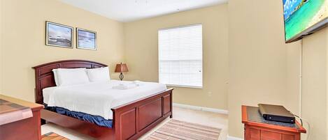 A bedroom with a bed, a ceiling fan, a TV mounted on the wall, and a window with blinds.