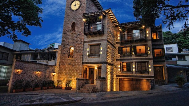 Un edificio de varios pisos con una torre de reloj, balcones y fachada de piedra.