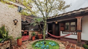Un patio con piso de ladrillo, una hamaca, un pequeño árbol y una zona de parrilla.