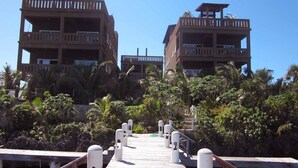 A wooden pier leading to a resort with multiple-story buildings, surrounded by lush greenery. - Luxury Waterfront Condo w/ Pool,  Dock, and Gardens  (West End)