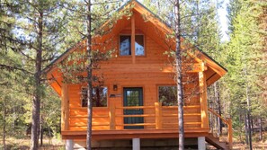 Une cabane en bois dotée d’un balcon, entourée d’arbres.