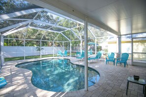 A covered outdoor swimming pool with a curved edge, surrounded by blue chairs and a small table.