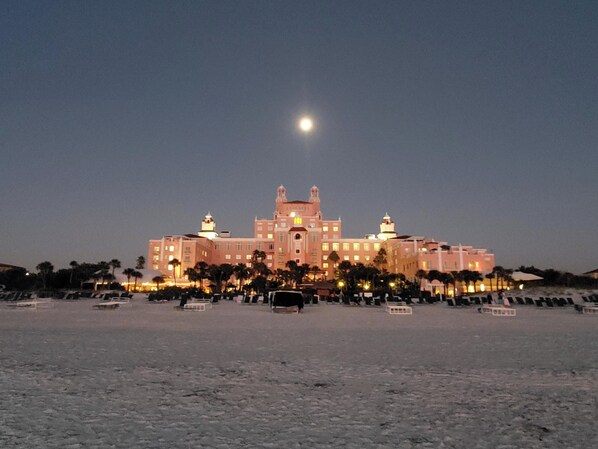 A large, multi-story building with a central dome and two smaller domes on either side, surrounded by palm trees and a sandy foreground.