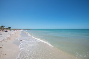 A beach with clear blue water, sandy shore, and a few people in the distance.