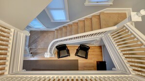 Eine moderne Treppe mit weißen Geländern, einem Holzboden und zwei schwarzen Stühlen oben.