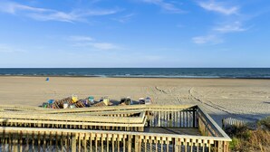 Ein Strand mit einer Holzpromenade, die zu einem Gebäude mit mehreren Zimmern führt.
