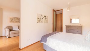 Een slaapkamer met een bed, een dressoir, een nachtkastje, een raam en een deur.