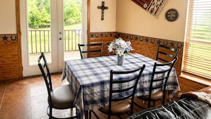 A dining area with a table set for four, a wooden bench, a decorative wall hanging, and a door leading to an outdoor deck.