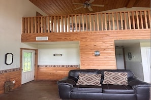 A room with a black leather sofa, a wooden ceiling, and a small window with a decorative glass door.