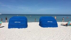 A beach with two blue covered chairs labeled "AMI CHAIRS" and a sandy beach area. - Oceanfront! Heated Pool! Free WiFi & Cable! Bidets! Deluxe Outdoor Kitchen! Oceanway 203! (Indian Rocks Beach)