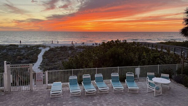 A beachside patio with lounge chairs and a view of the ocean at sunset. - Oceanfront! Heated Pool! Free WiFi & Cable! Bidets! Deluxe Outdoor Kitchen! Oceanway 203! (Indian Rocks Beach)