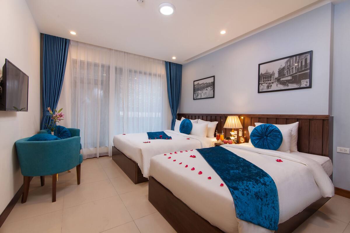 A hotel room with two beds, a TV, a chair, and a window with curtains.