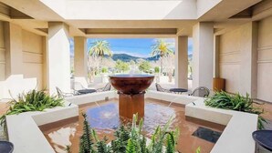 Ein moderner Innenhof mit einem zentralen Wasserspiel, umgeben von Sitzgelegenheiten und Pflanzen, mit Blick auf eine gebirgige Landschaft.