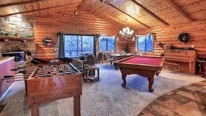 A cozy log cabin interior with a pool table, foosball table, and a dining area.