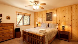 A bedroom with a wooden bed, two bedside lamps, a ceiling fan, a dresser, a window, and a framed picture on the wall.