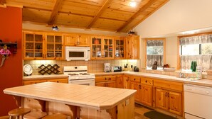 A kitchen with wooden cabinets, a central island with stools, a microwave, stove, and a dishwasher.