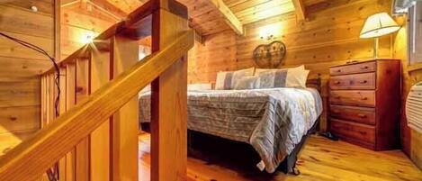 A wooden cabin bedroom with a bed, dresser, and a staircase.