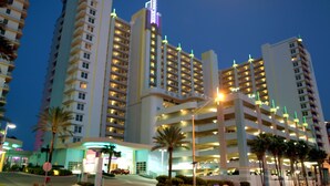 Un hôtel à plusieurs étages, doté d’une enseigne lumineuse bien visible, de plusieurs parkings et de palmiers au premier plan.