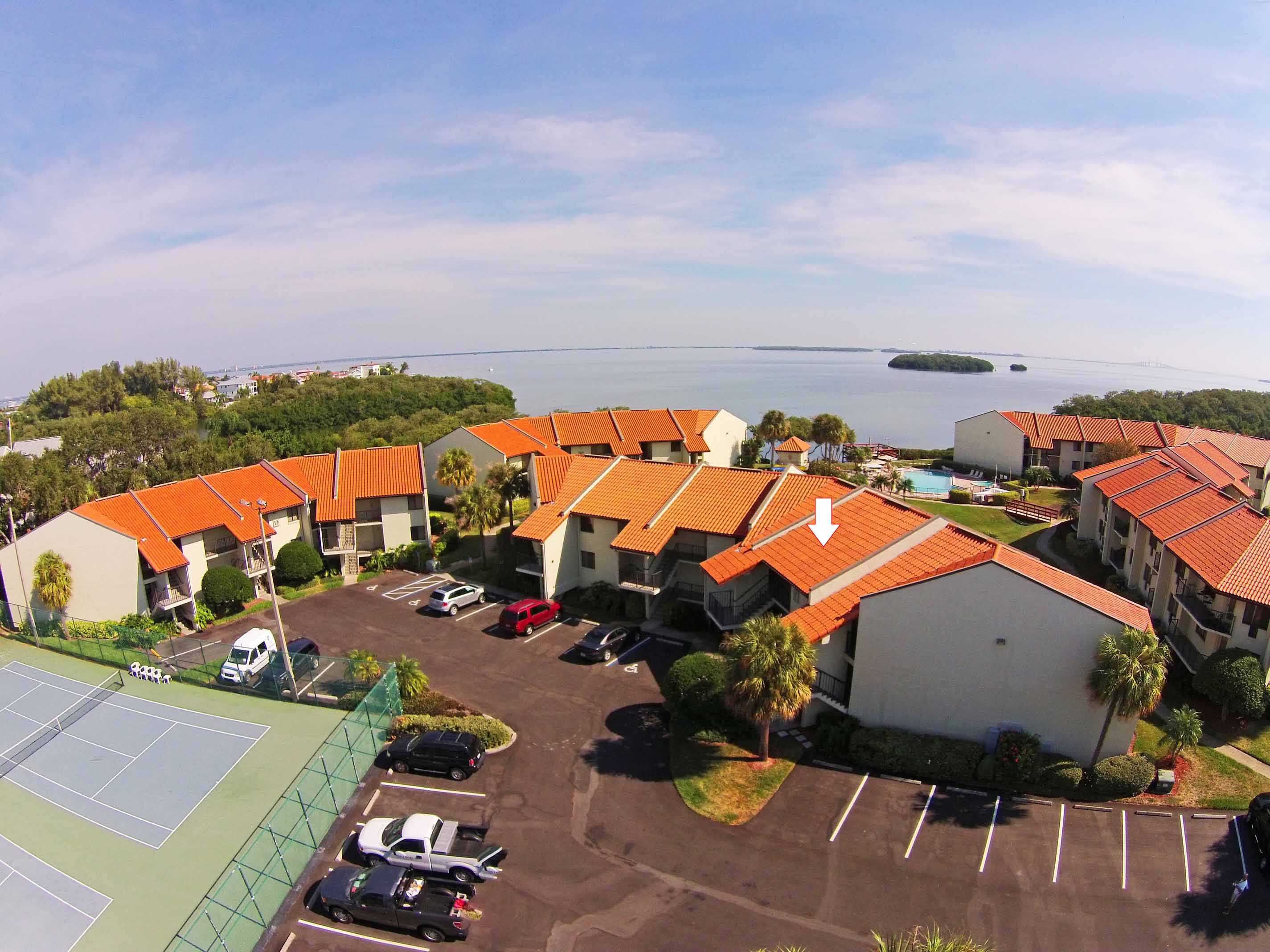 A coastal hotel with multiple buildings, a parking lot, and a tennis court.