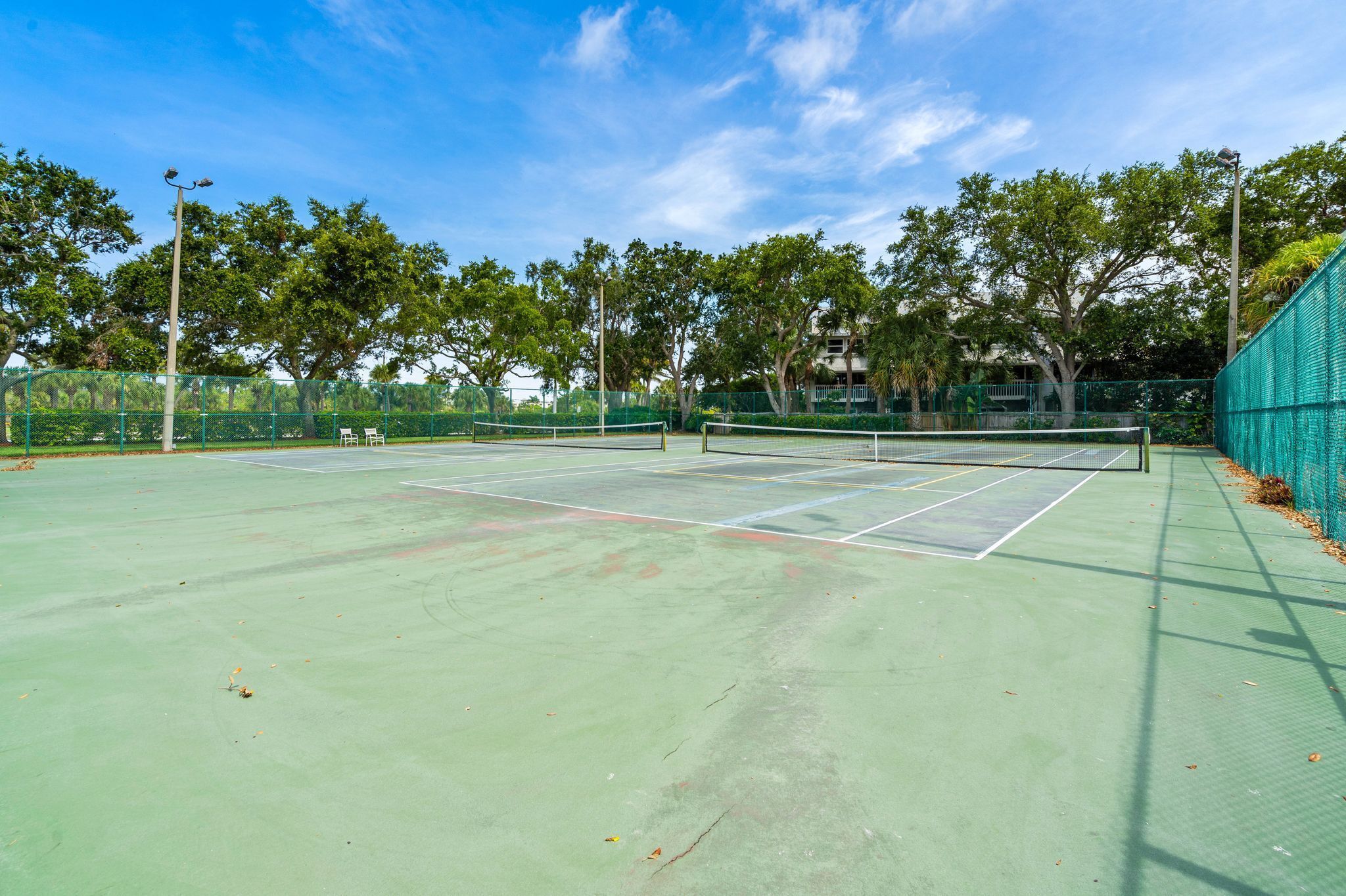 An outdoor tennis court with a net, surrounded by trees and a fence.